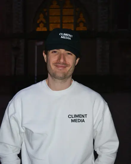 Manuel Climent, smiling, in a Climent Media cap and white sweatshirt, outside a church at night